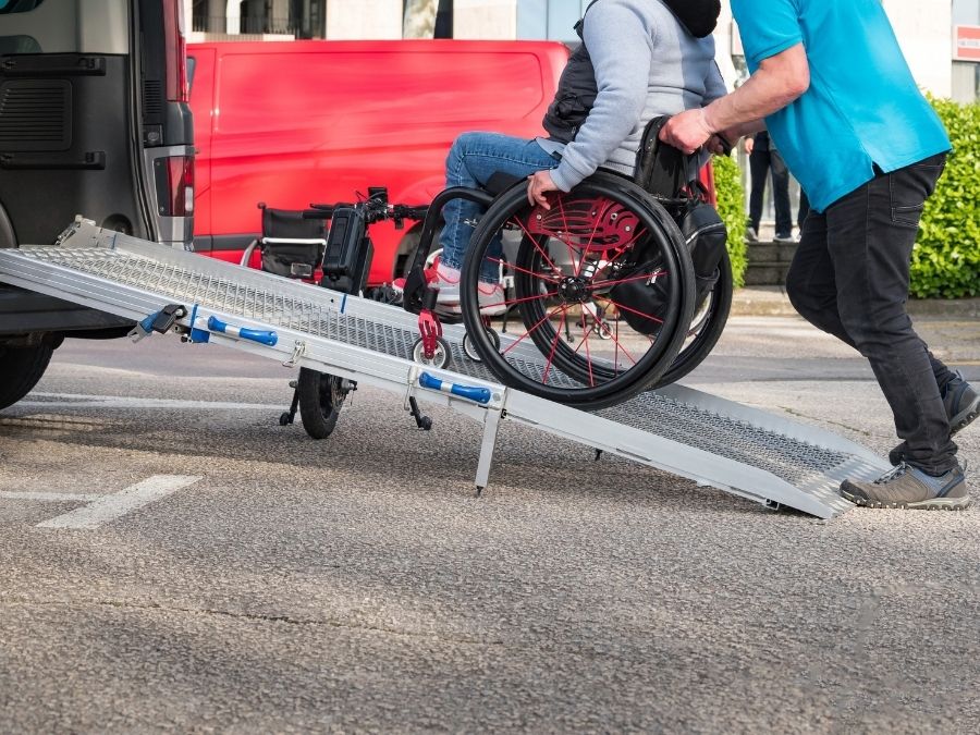 A wheelchair users i pushed up a ramp into a wheelchair accessible minibus